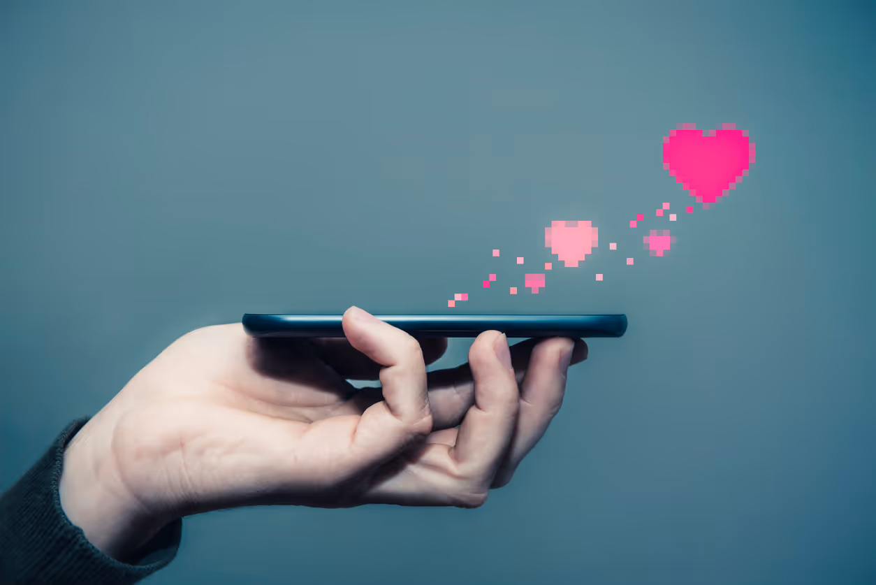 Eine Hand hält ein Handy, aus welchem verpixelte Herzen schweben.