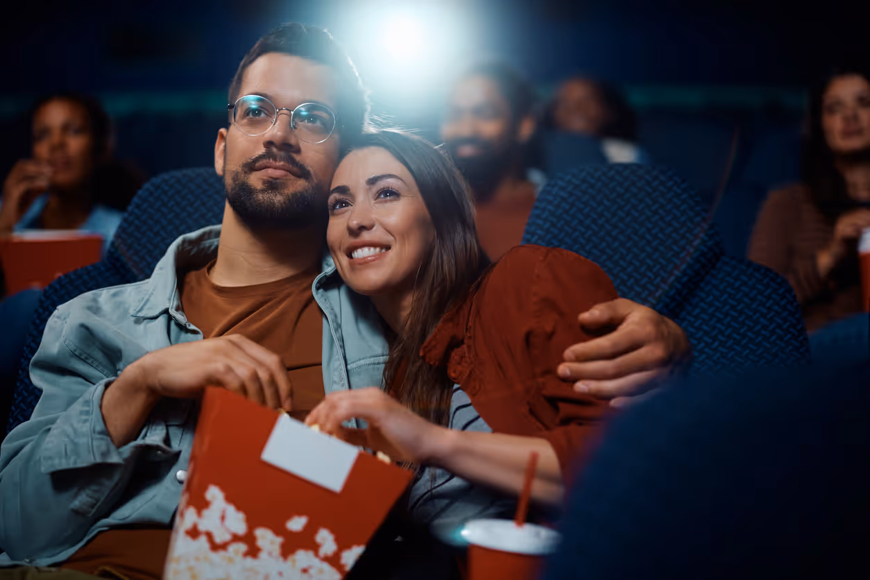 Paar sitzt entspannt Rücken an Rücken im Kino, teilt Popcorn und schaut einen Film.