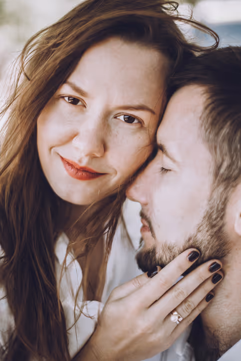 Eine Frau und ein Mann, deren Gesichter aneinander liegen. Die Frau blickt in die Kamera und berührt das Gesicht des Mannes.