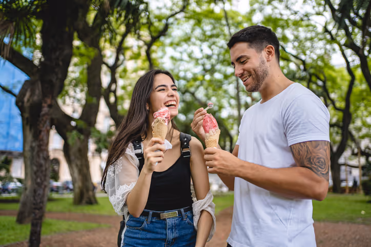 Junge Frau und Mann mit Eis in der Hand vor grünen Bäumen