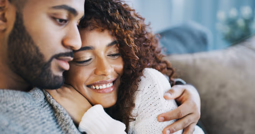 Ein junges Paar umarmt sich auf dem Sofa und genießt den Moment der Nähe.