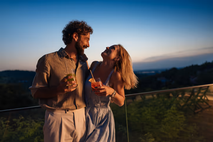 Paar genießt Cocktails auf dem Balkon bei Sonnenuntergang