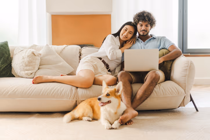 Junges Paar entspannt sich auf einem Sofa mit ihrem Hund und einem Laptop