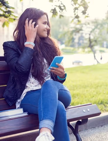 Frau lächelt mit einem Handy in der Hand auf einer Bank sitzend