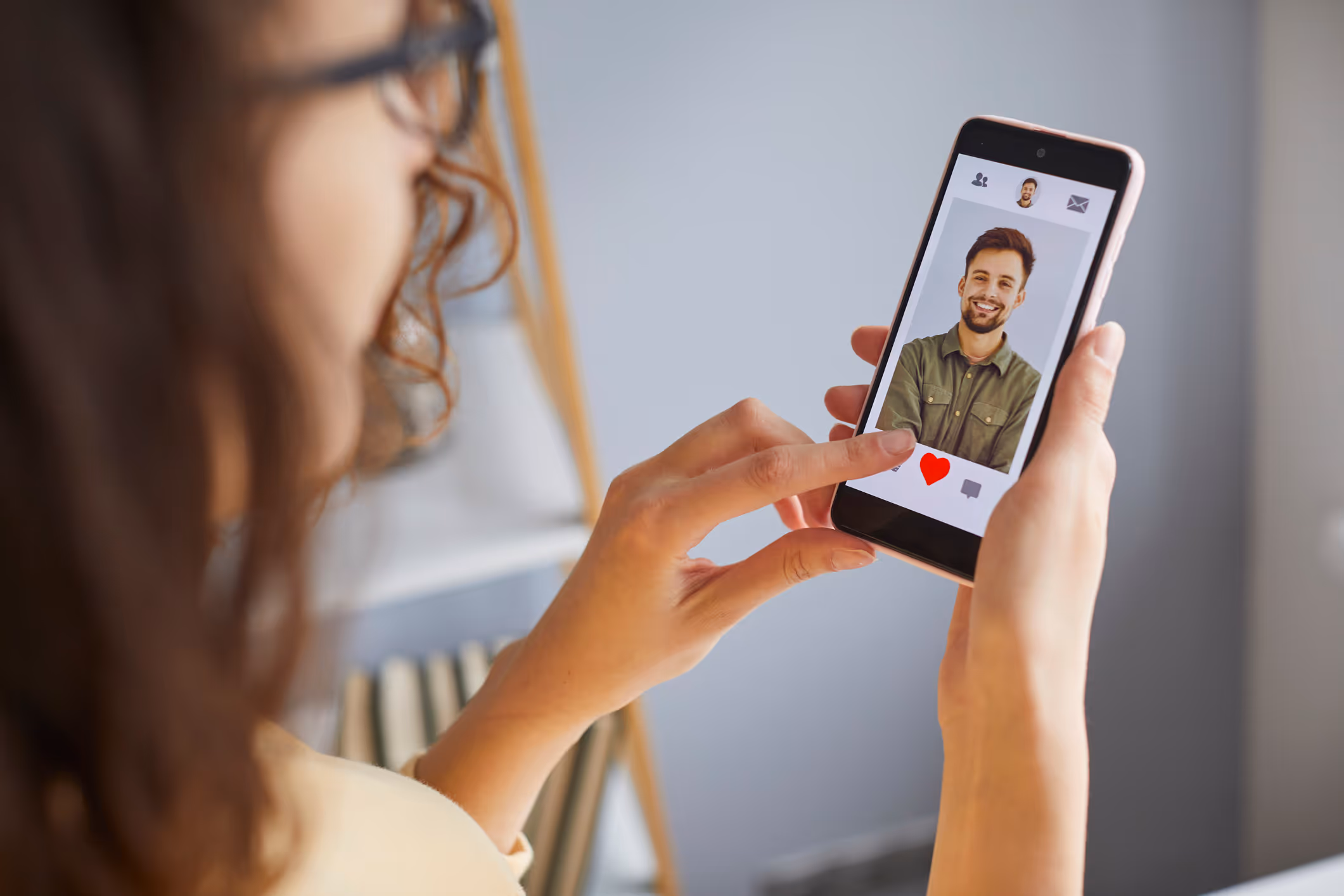 Frau nutzt eine Dating-App auf ihrem Smartphone und tippt auf das Herzsymbol unter einem Profilbild