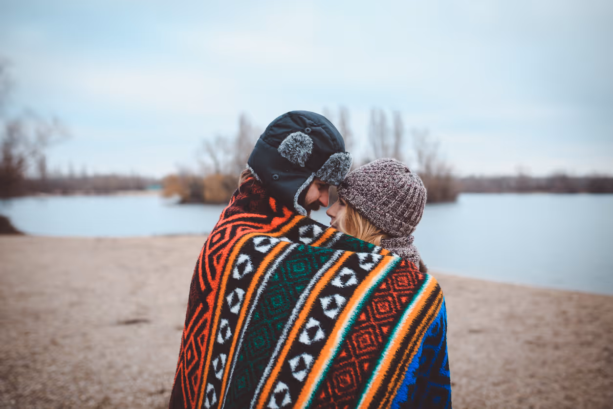 Verliebtes Paar kuschelt unter Decke im Winter am See