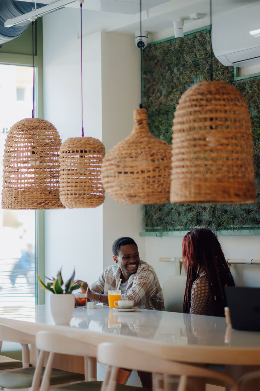 Zwei Personen sitzen in einem modernen Café mit Rattanlampen und genießen Getränke