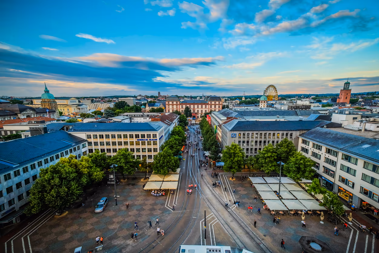 Blick von oben auf eine belebte Innenstadt mit Straßenbahnschienen, Plätzen, Bäumen und umliegenden Gebäuden