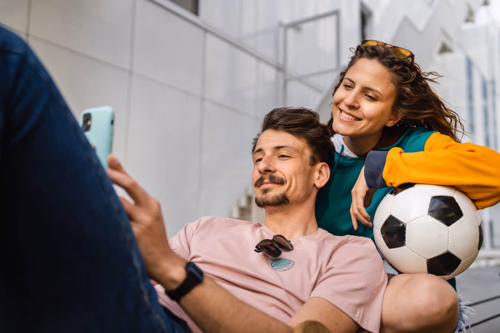 Fröhliches Paar sitzt draußen und posiert für ein Selfie mit einem Fußball in der Hand