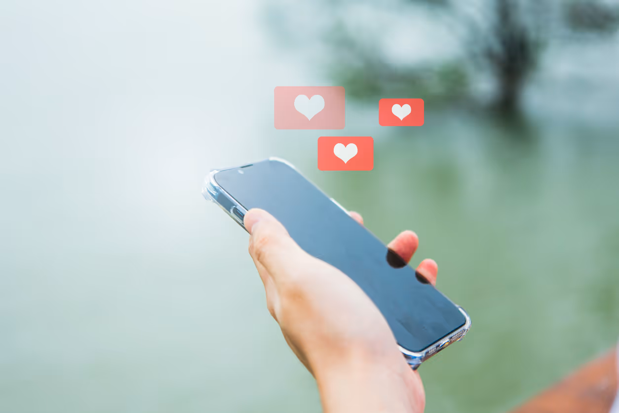 Person hält ein Smartphone mit Herz-Symbolen im Vordergrund, auf unscharfem Hintergrund.