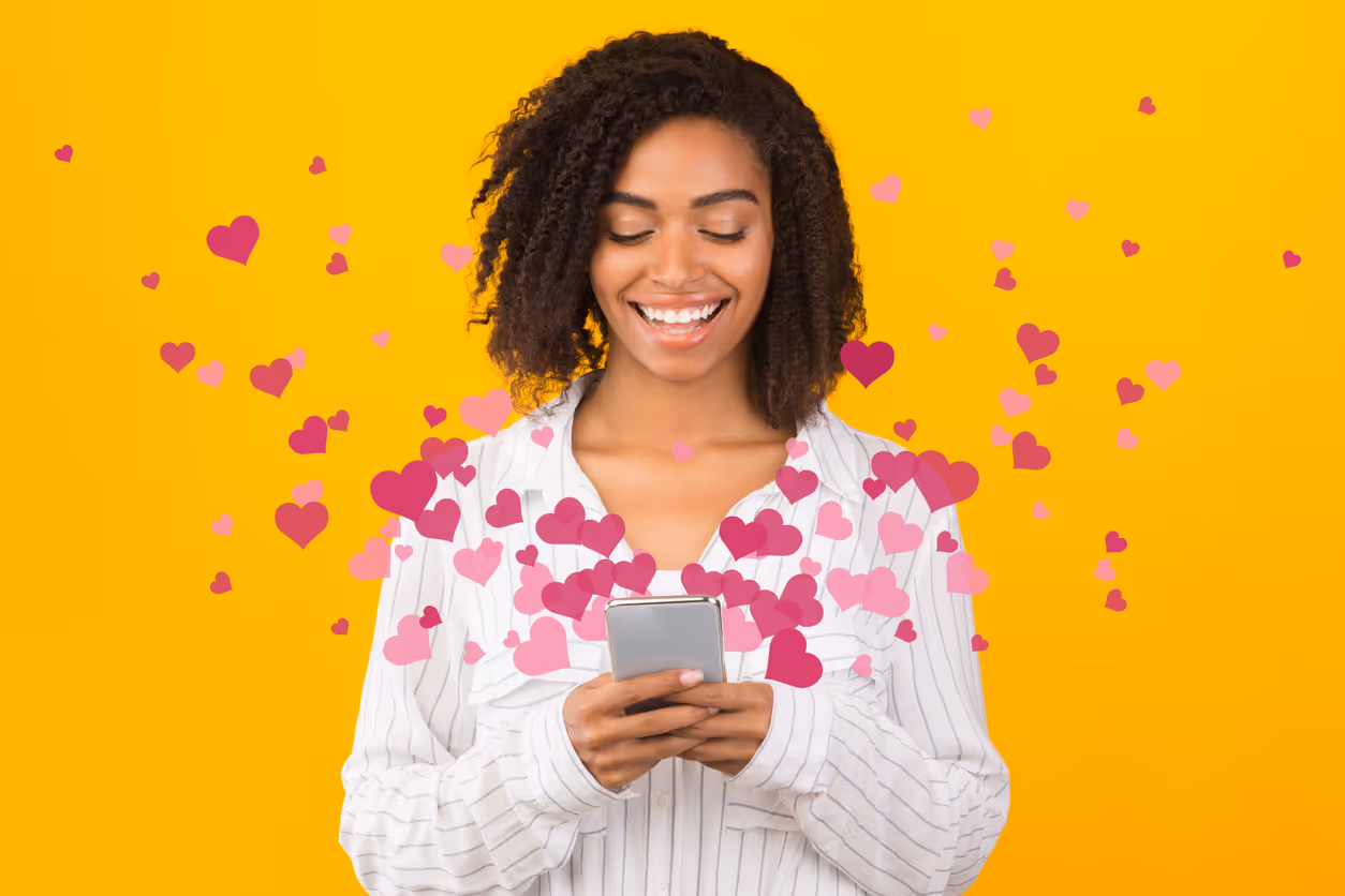 Person steht vor gelbem Hintergrund und nutzt ein Smartphone, umgeben von schwebenden Herzgrafiken.