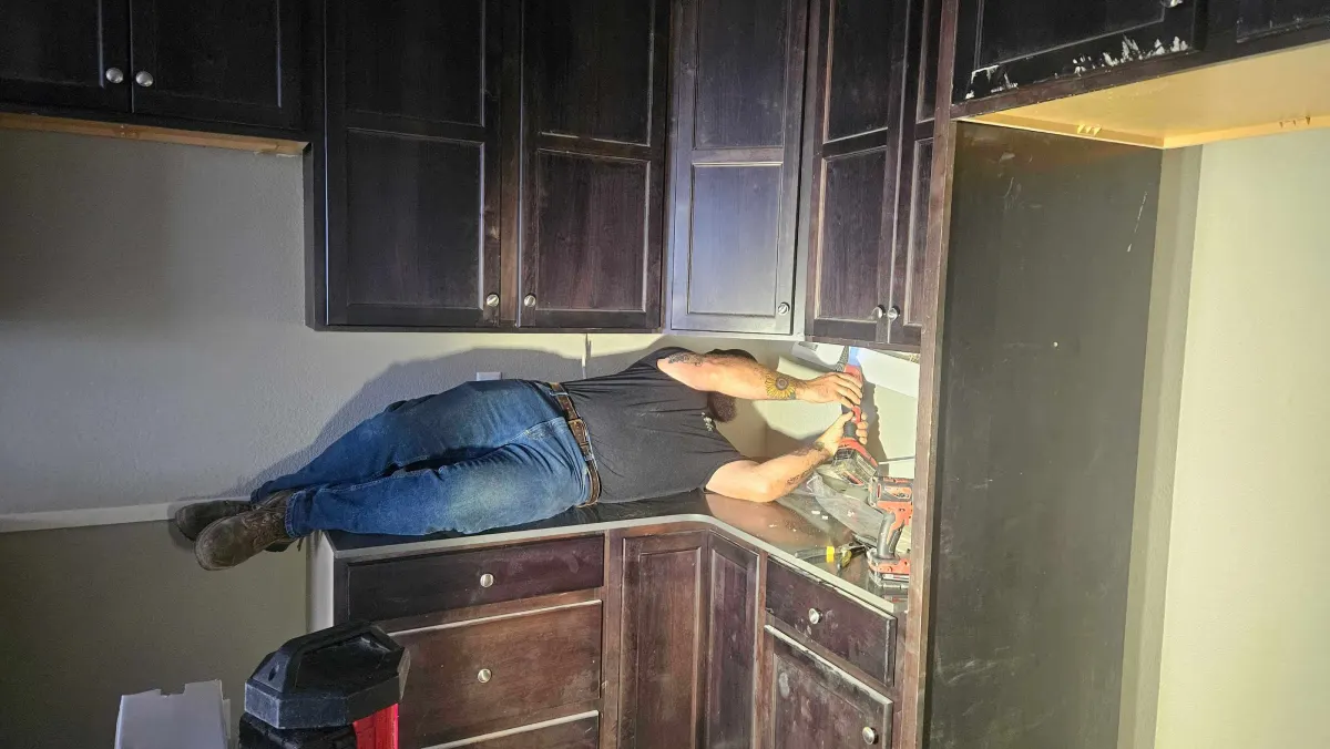 Person working inside kitchen cabinet with tools and shop vacuum nearby