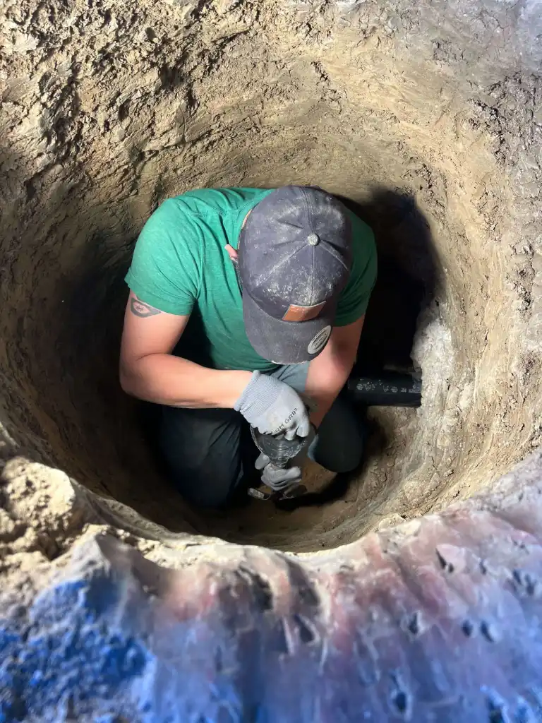 Worker in green shirt digging and working inside a deep earthen hole