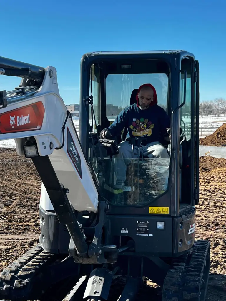 Operator driving Bobcat excavator on snowy construction site