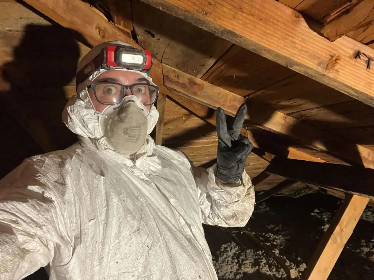 Worker in protective gear makes peace sign in dusty wooden attic space
