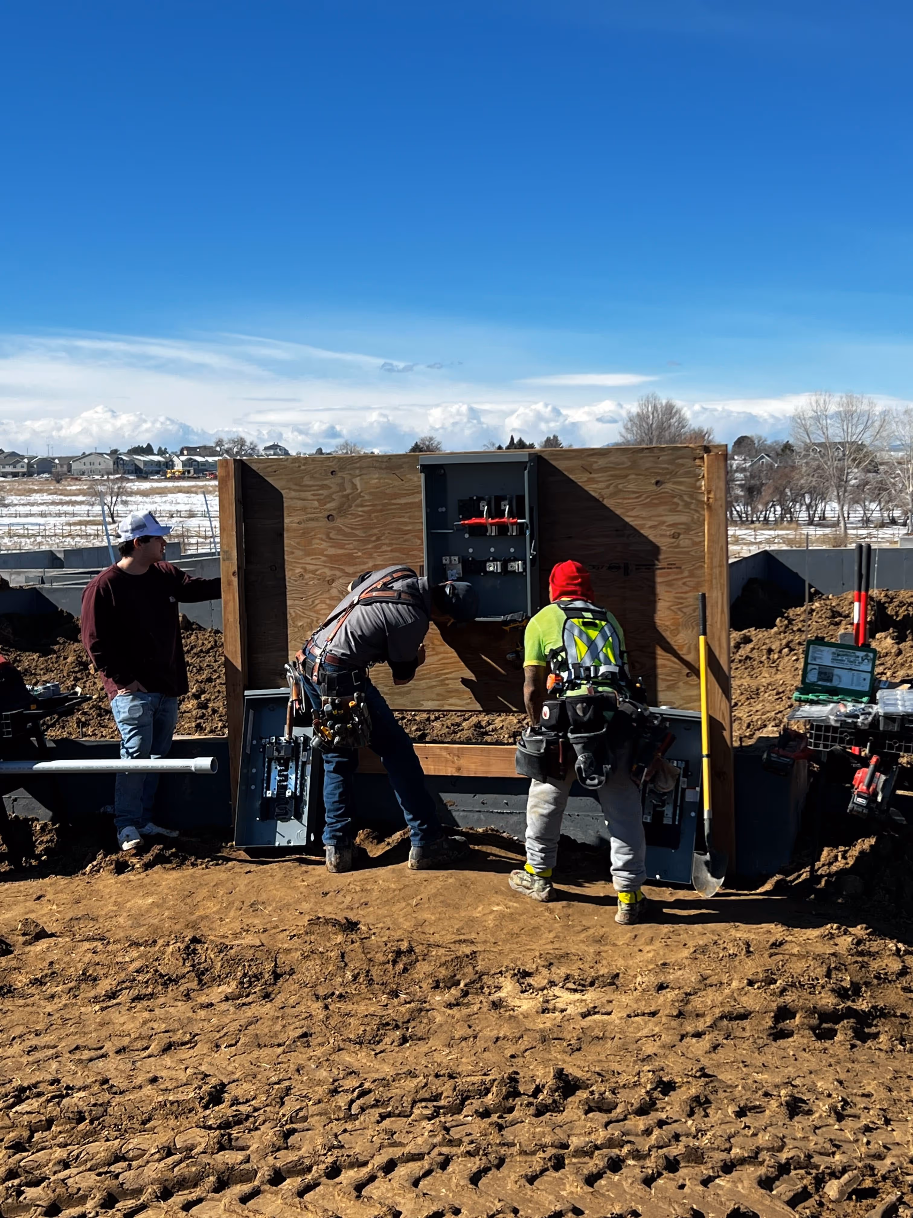 Construction workers installing electrical equipment on muddy building site