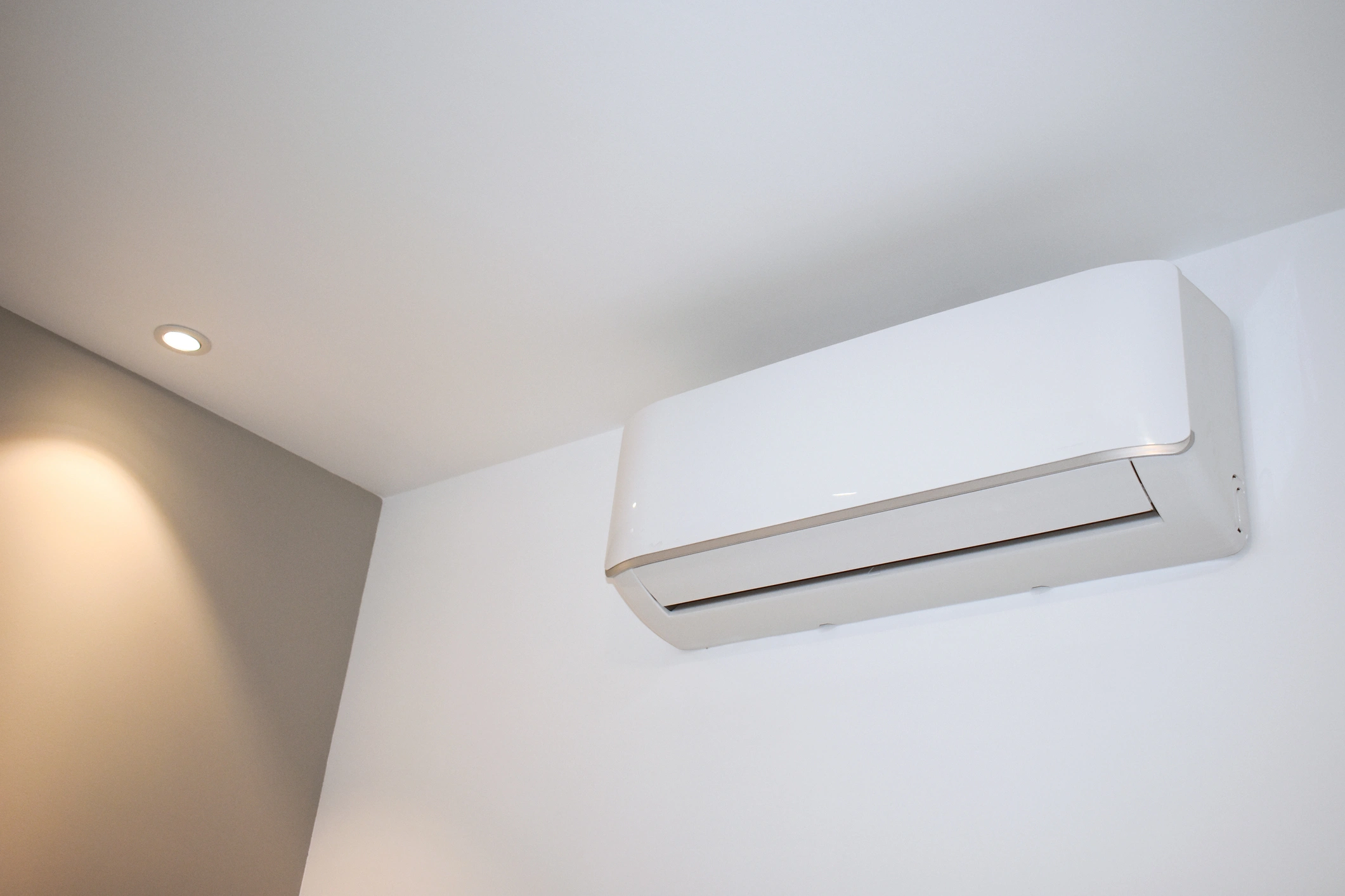 Minimalistic room corner showing a modern white air conditioner mounted on a light gray and white wall.