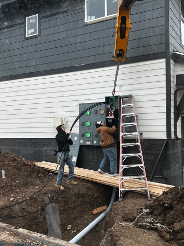 Workers installing electrical panel near house foundation with ladder