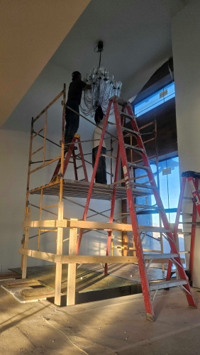 Worker on scaffolding installing chandelier in renovated interior