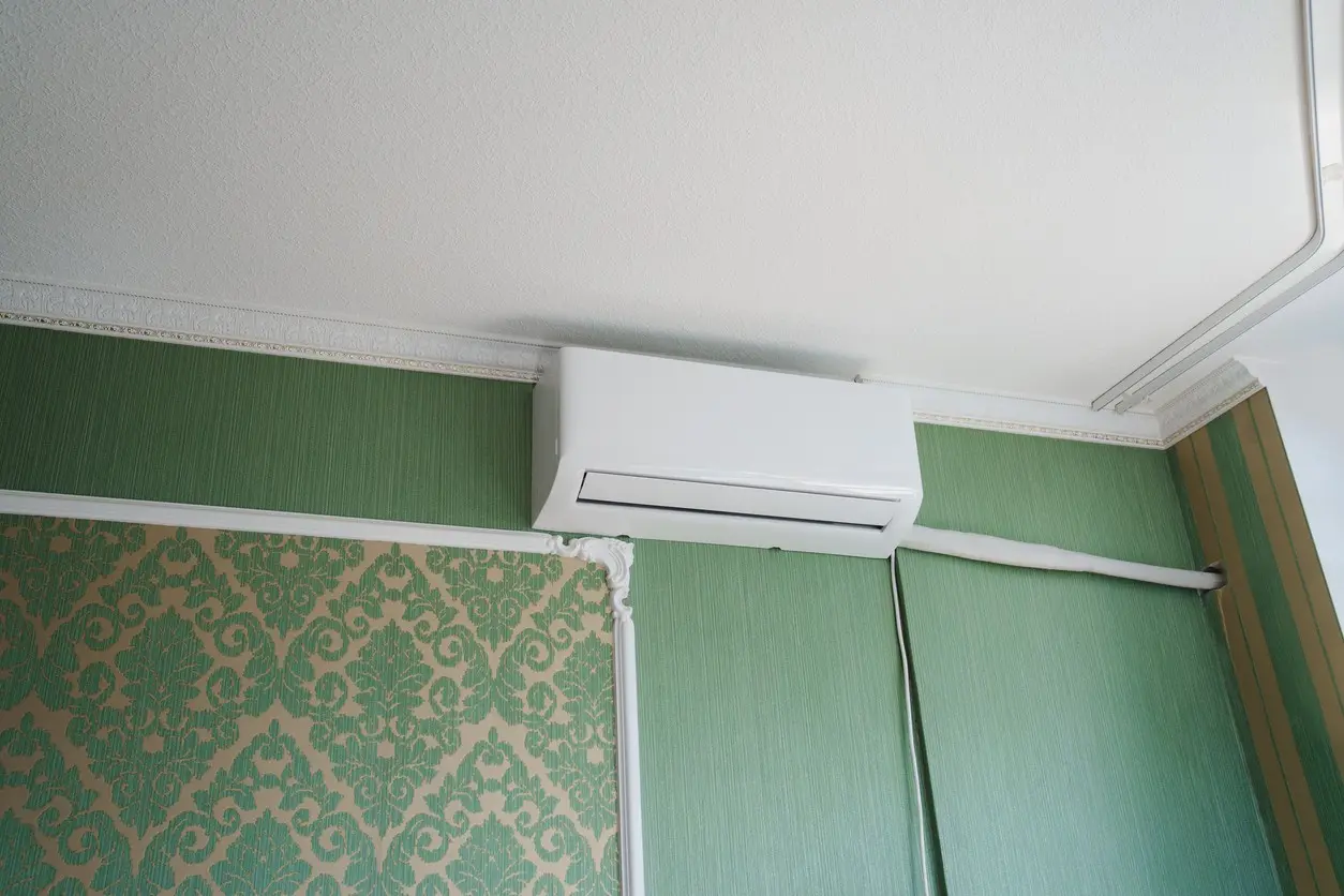 A person's hands are holding the lower part of a disassembled white mini-split AC unit in front of a window.