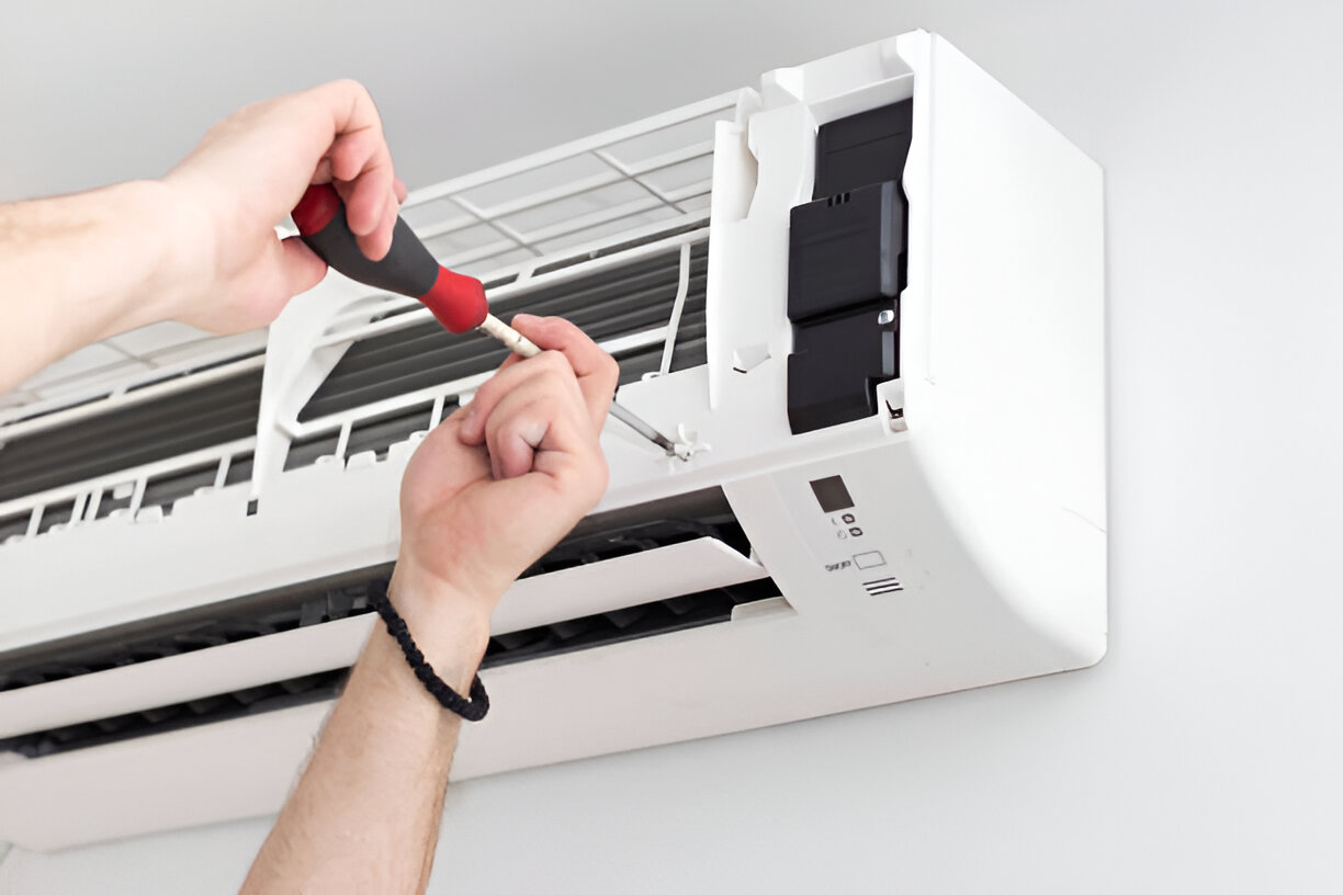 A hand uses a remote control to adjust the temperature settings of a white, wall-mounted ductless mini-split air conditioner.