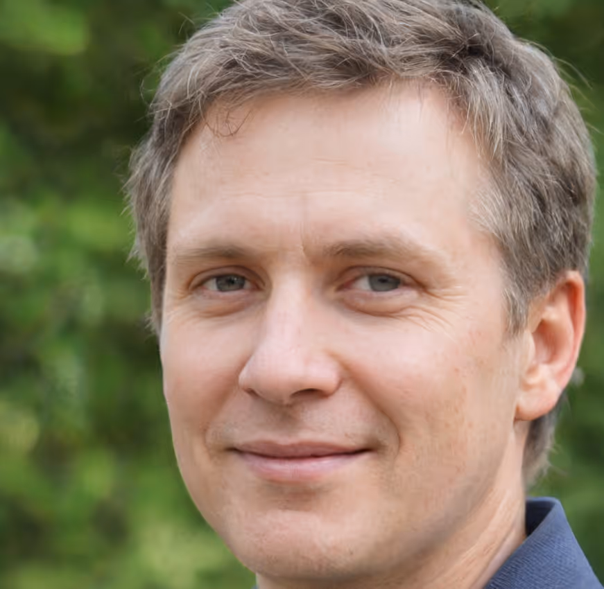Close-up of a smiling middle-aged man with light brown hair and blue eyes, outdoors with greenery in the background.