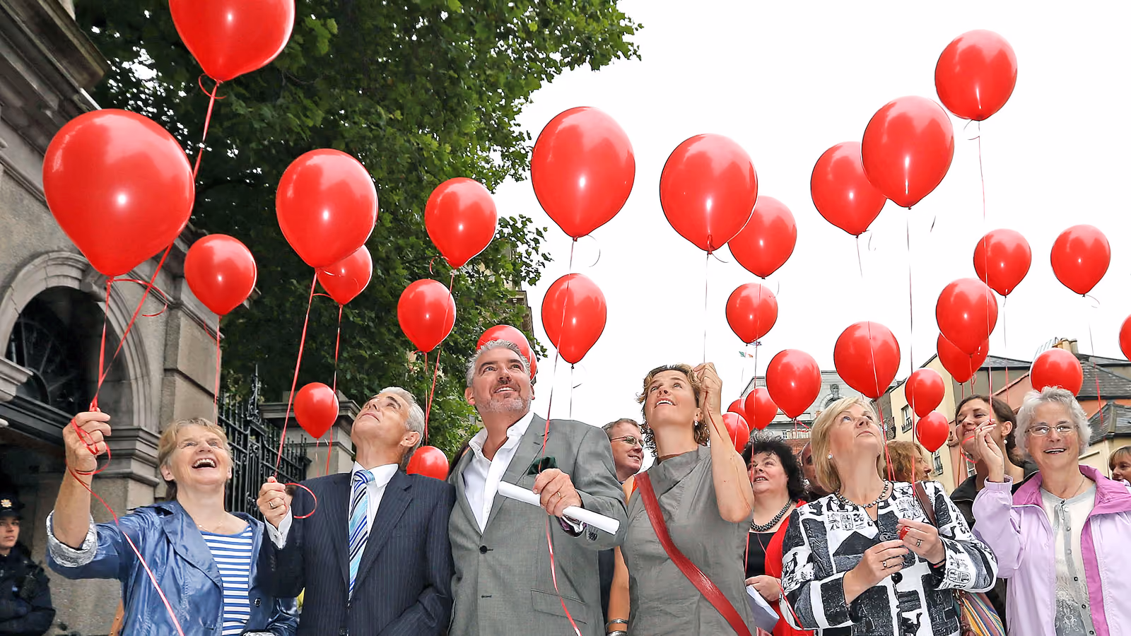 A group of people, all holding red balloons