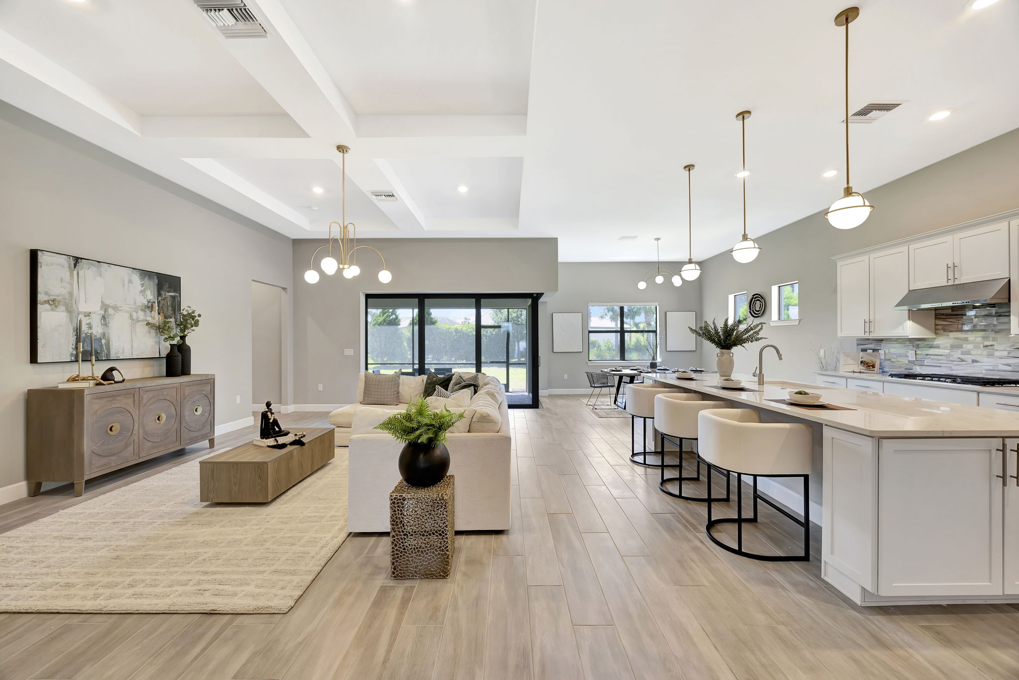 Modern open-plan living and kitchen area with sofa, kitchen island, bar stools, pendant lights, and elegant decor for luxu...