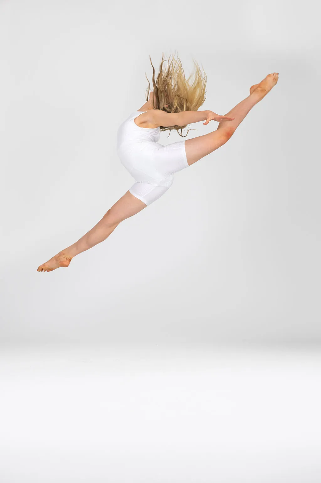 Danceology dancer in white mid-leap, front leg straight and back leg in attitude
