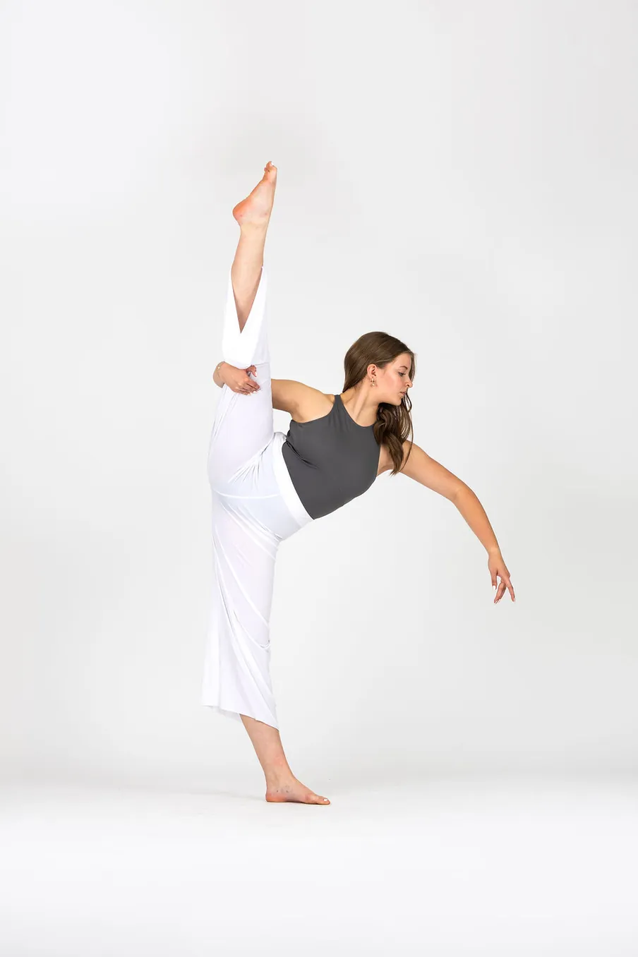 Danceology dancer in white pants holding a high extension with one arm reaching forward