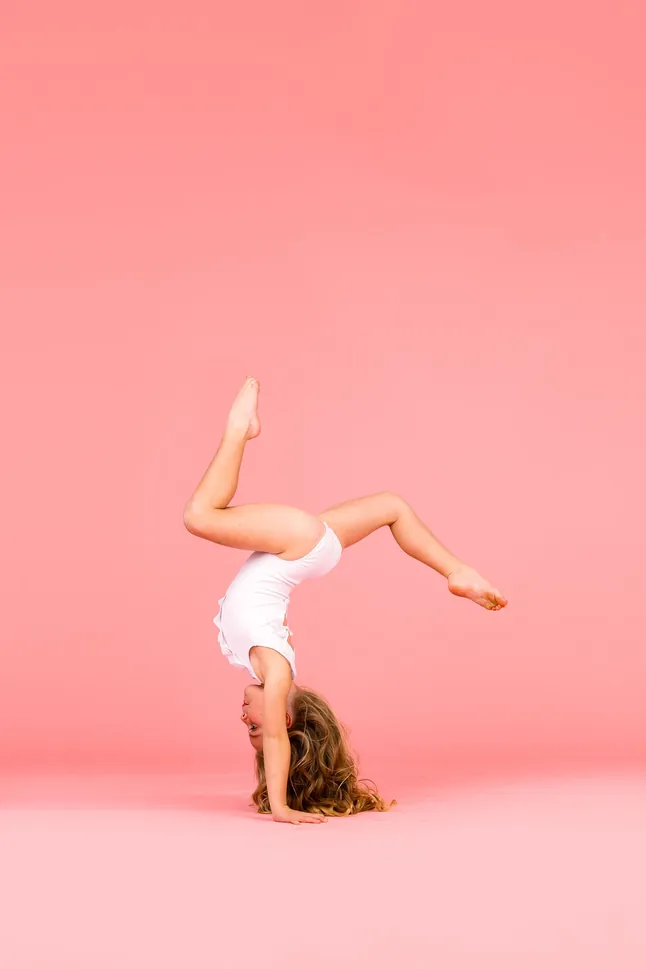 Danceology dancer in a handstand with legs in a stag shape on a coral backdrop