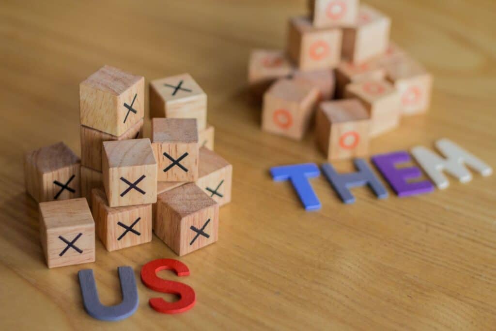Wooden blocks with X marks and colorful letters spelling 'US' and 'THEM'