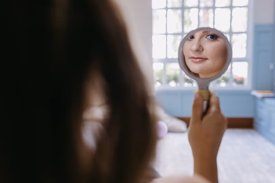A person with glowing, healthy skin looking happily in a mirror - why use medical grade skin care products