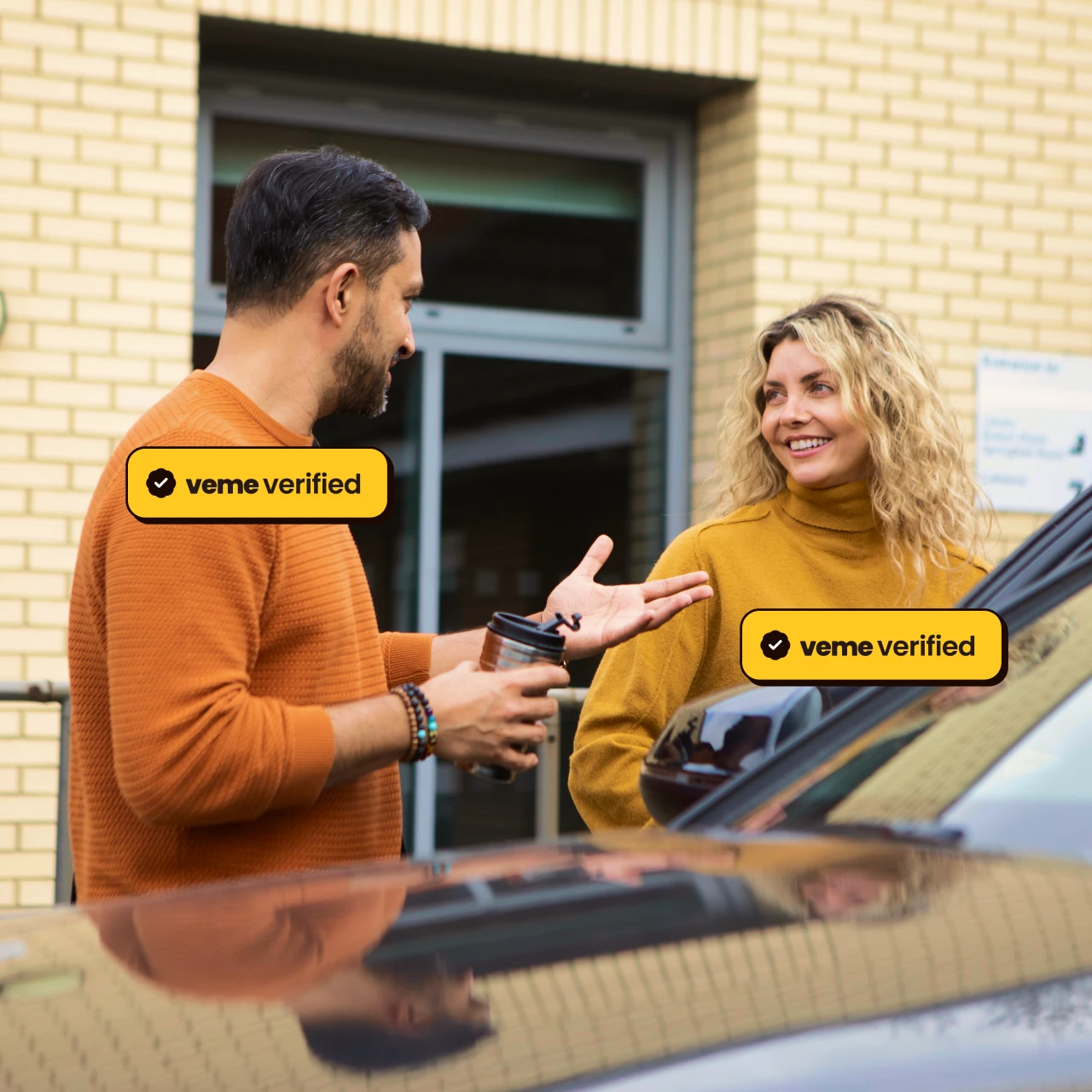 Man and woman smiling and conversing outdoors near a car, both wearing mustard and orange sweaters.