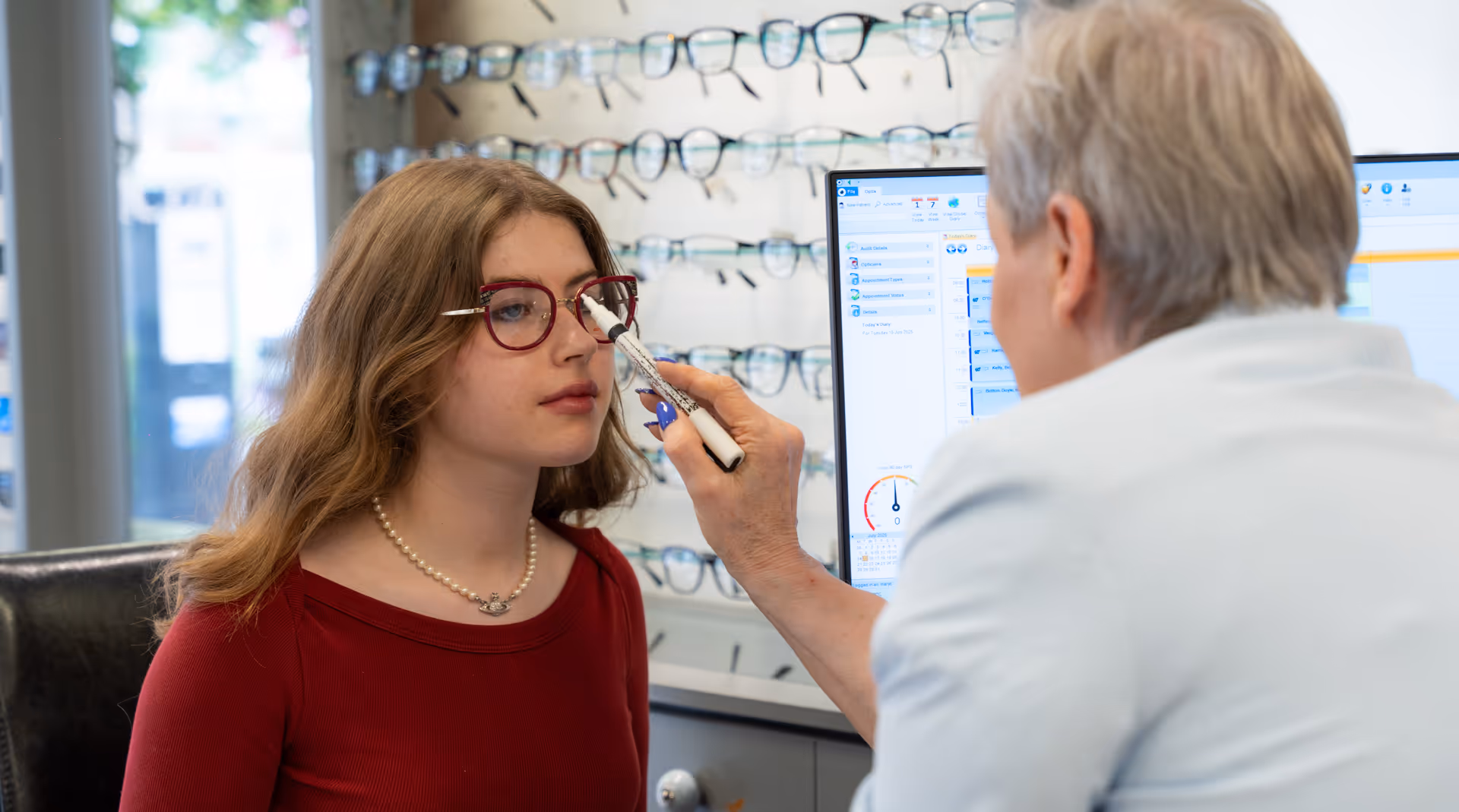 Eye doctor performs eye exam with patient in optical store with glasses display