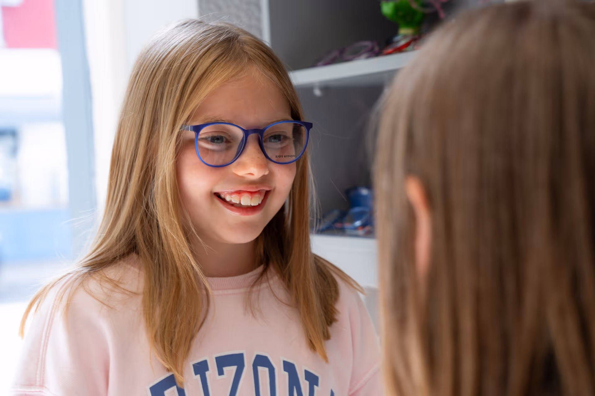 Young person with blue glasses smiling brightly in pink shirt