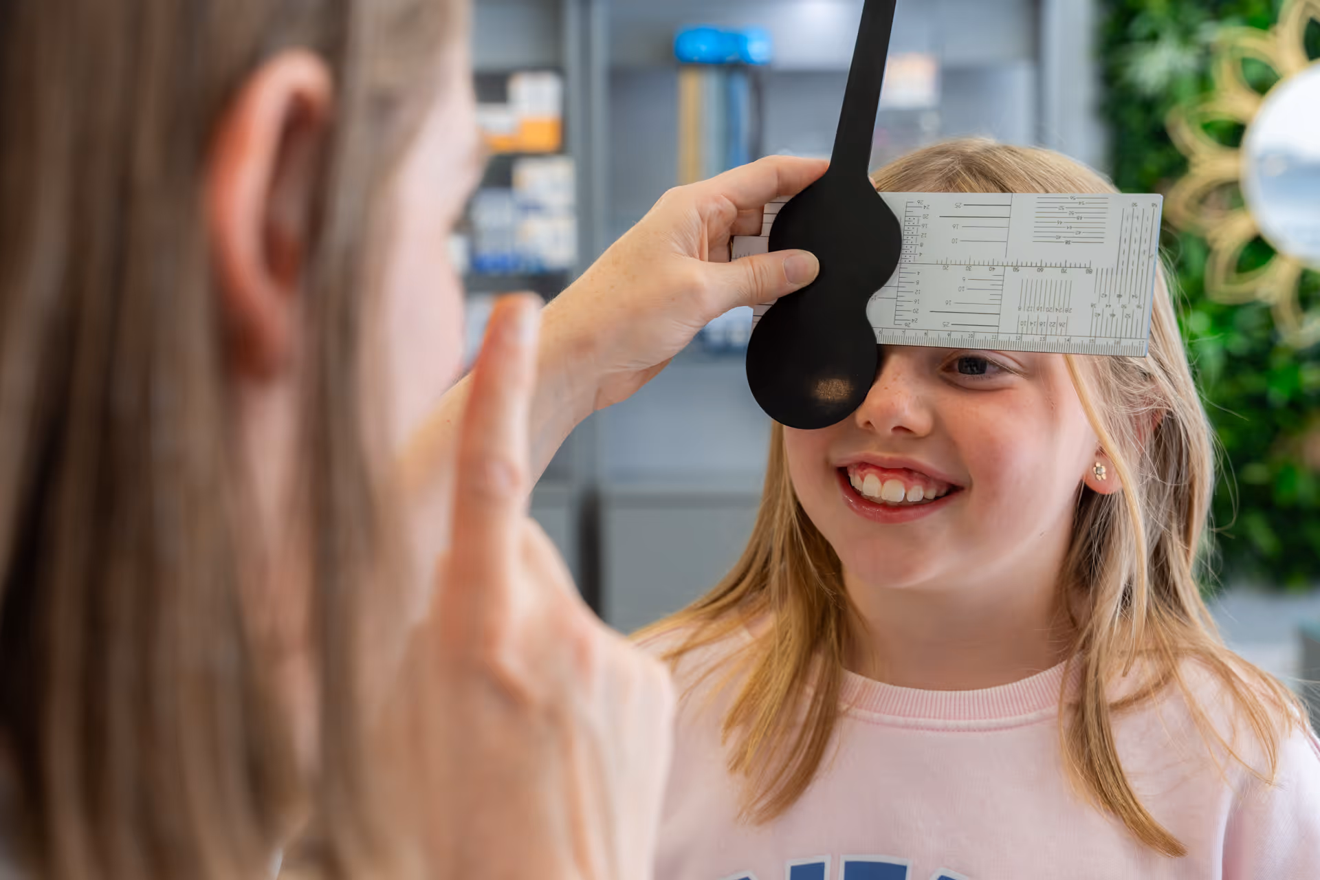 Child smiling during eye exam with occluder and measurement chart