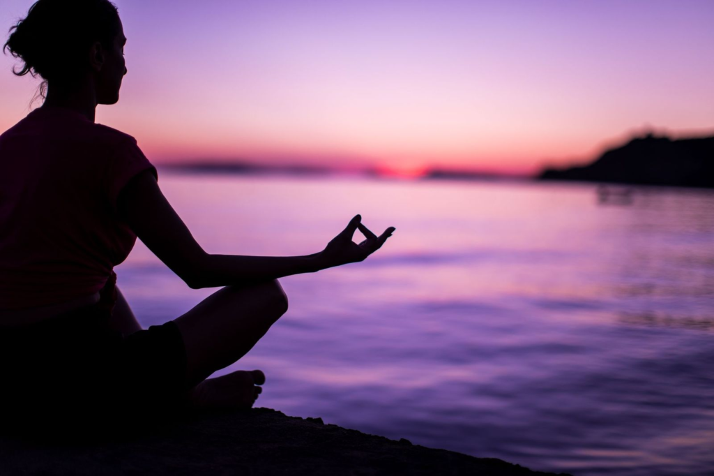 Person meditating next to the ocean at sunrise
