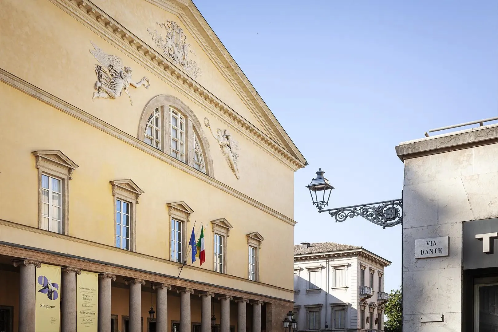 Facciata di un palazzo storico di Parma con colonne, bandiere e lampione d'epoca.