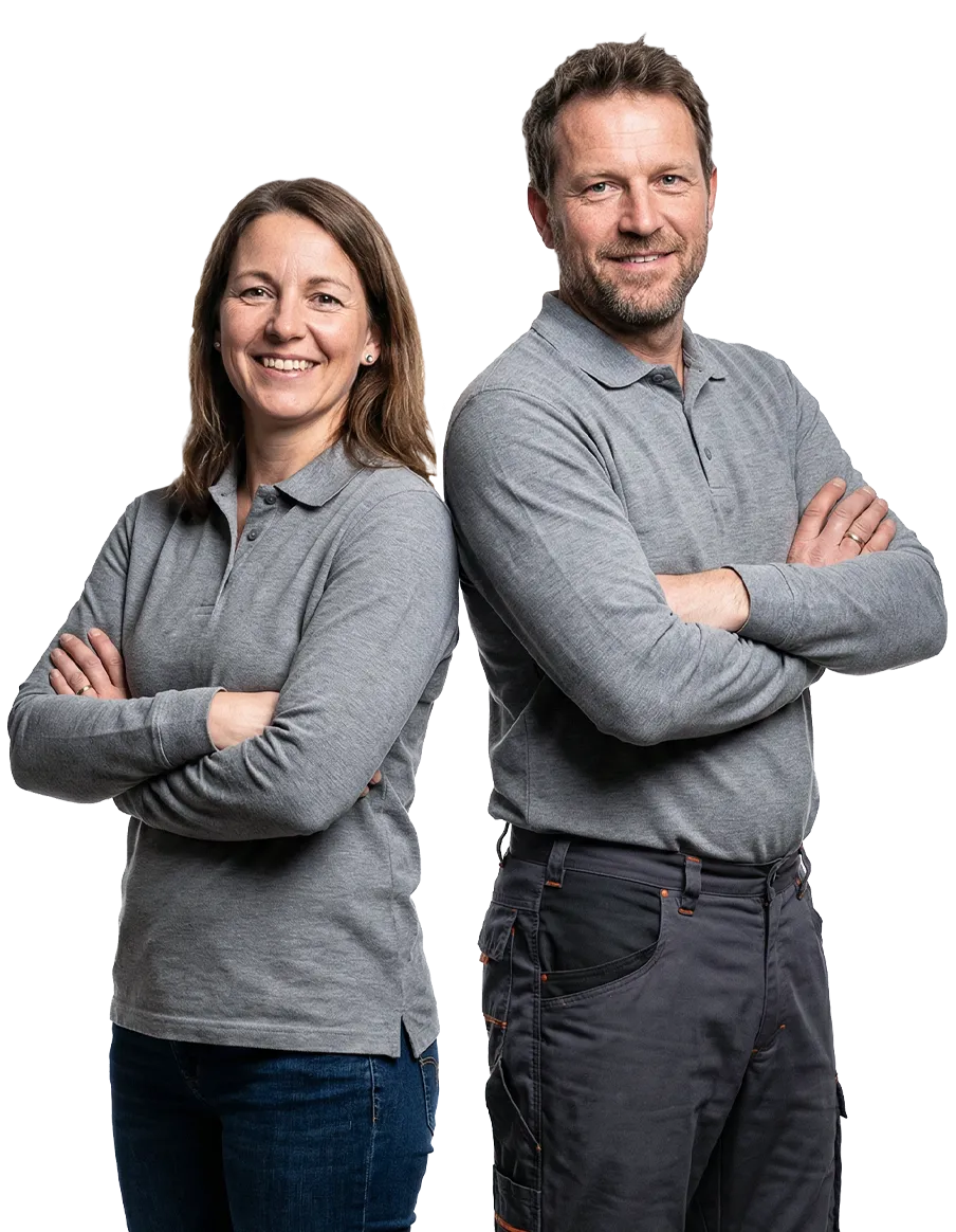 Eine weibliche Ausbilderin sowie ein männlicher Ausbilder in Arbeitsmontur wie diese Rücken an Rücken mit verschränkten Armen stehen und lächeln.
