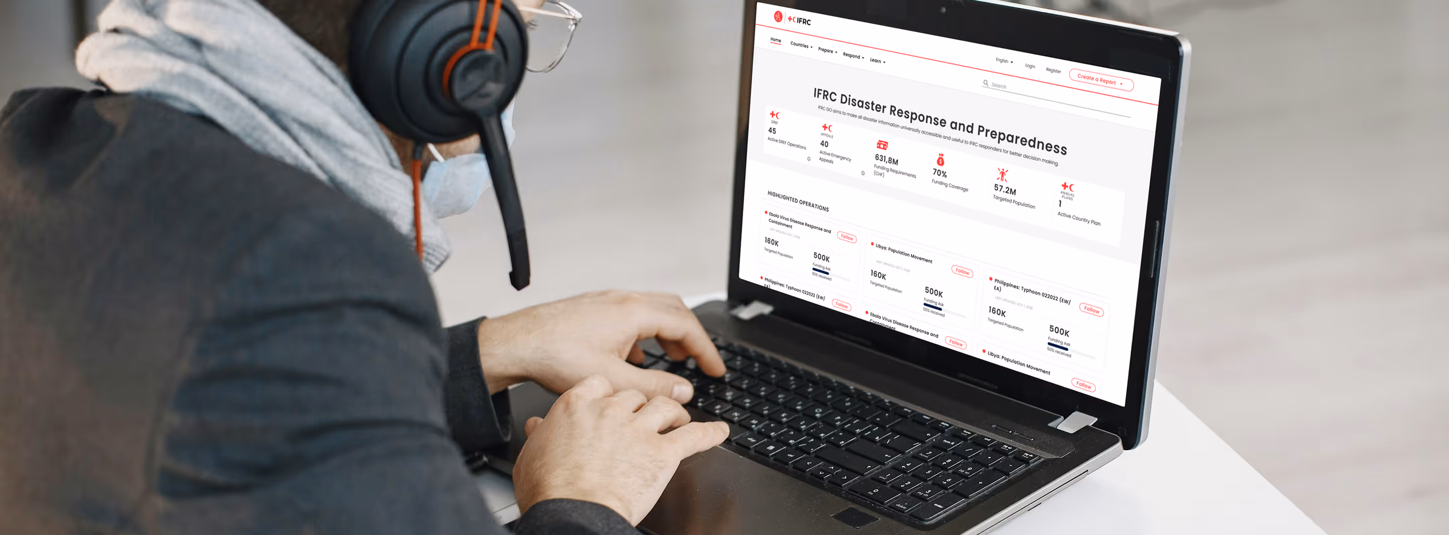 Person working on a laptop, wearing a headphone with microphone and a mask. The screen has the IFRC GO application on the screen.