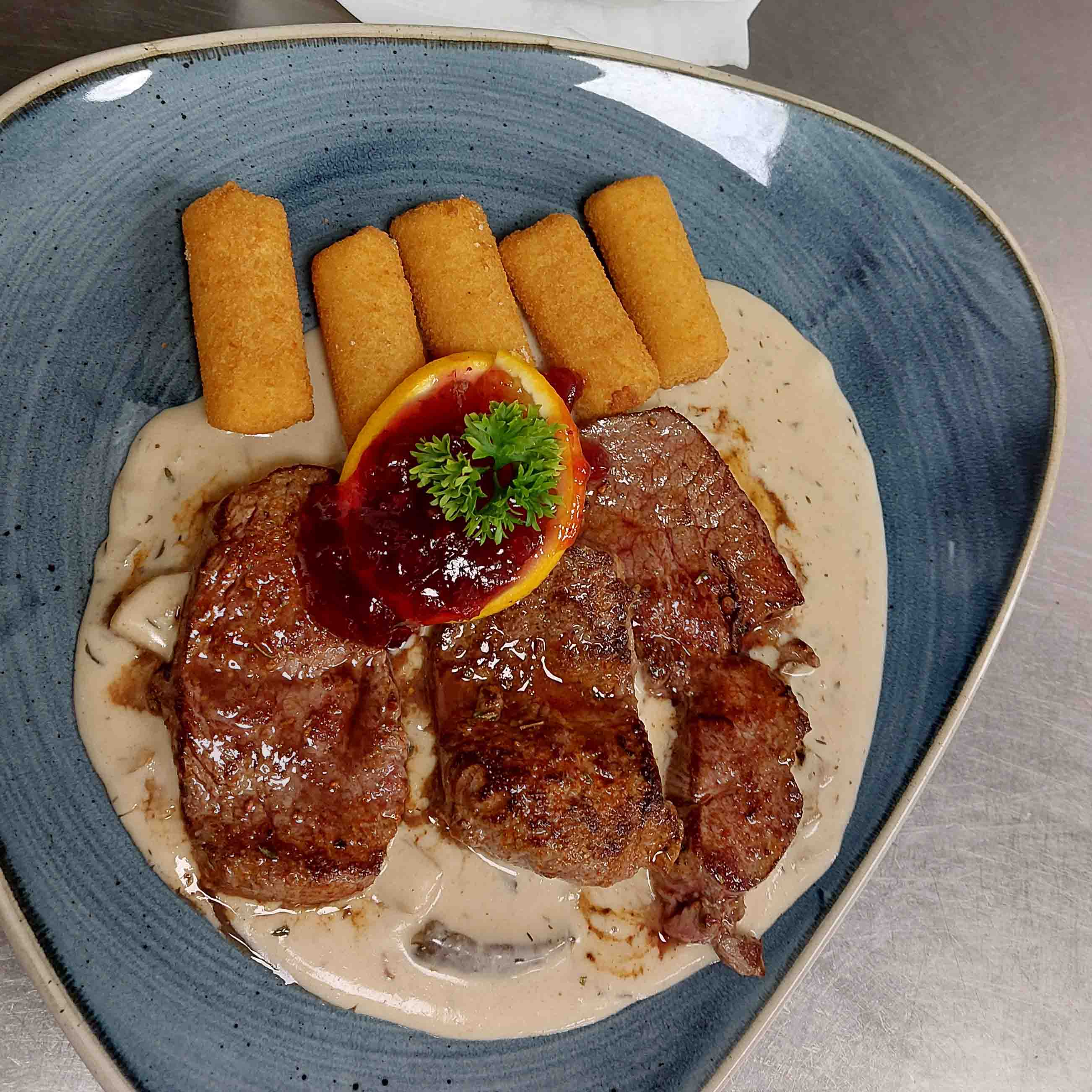 Wildschnitzel mit Beilage auf blauen Teller.