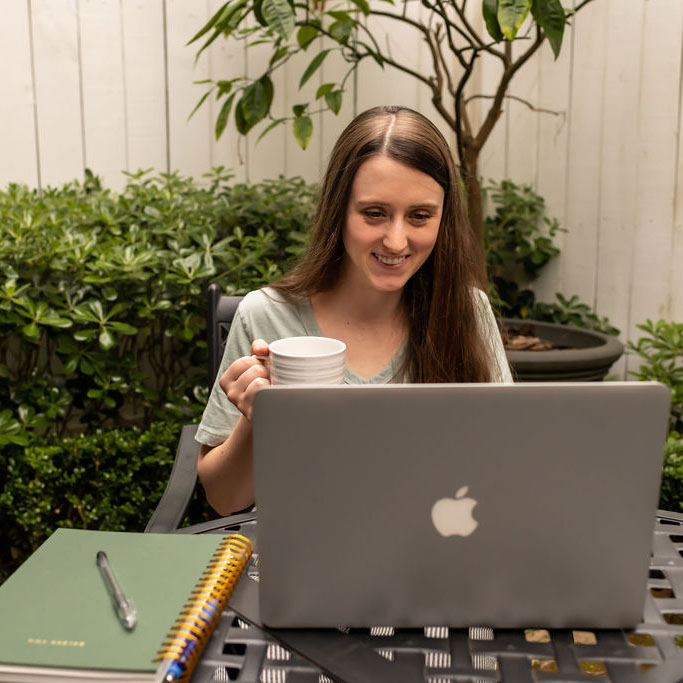 Woman holding coffee mug smiling in front of laptop computer