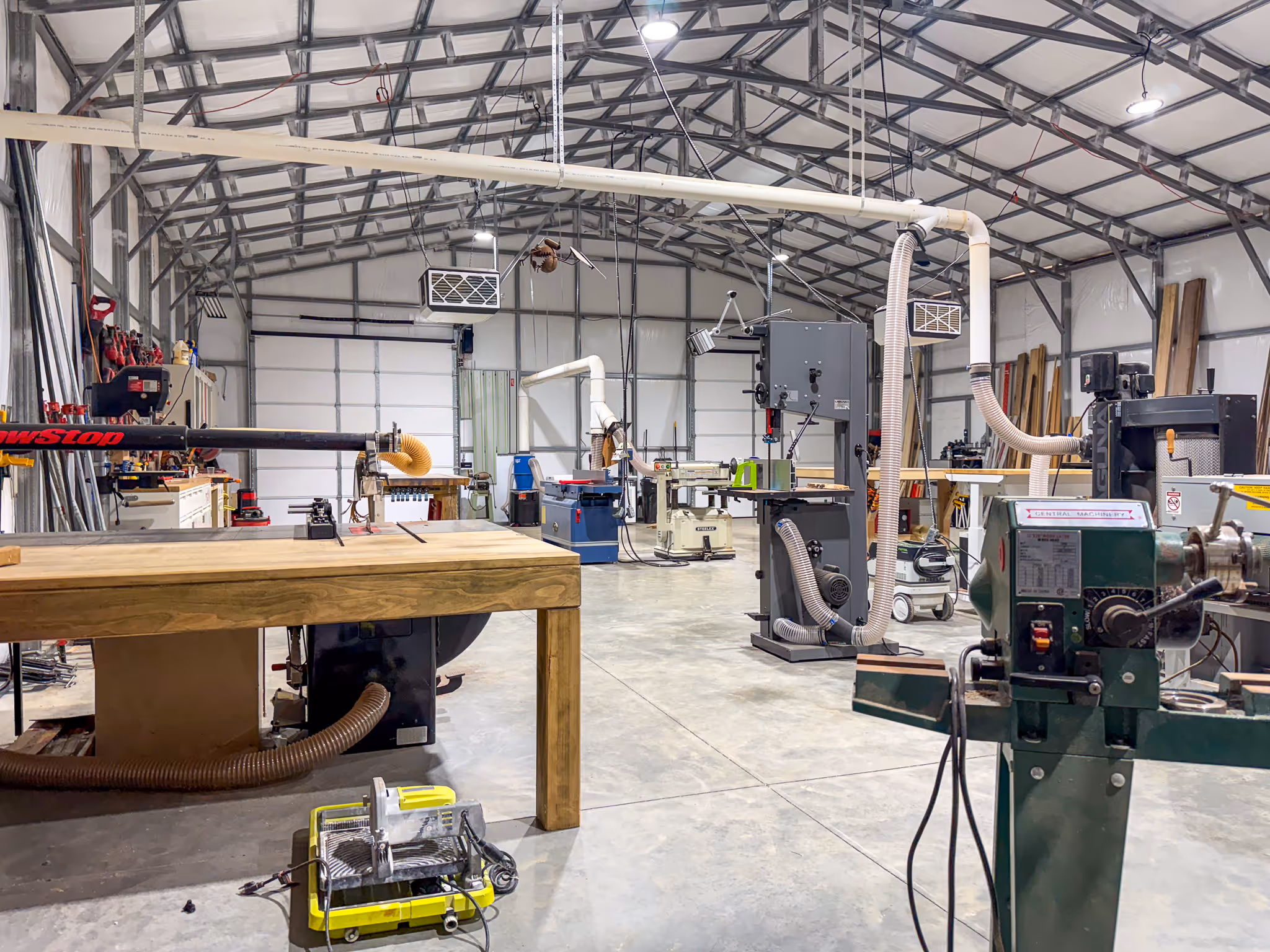 Nautilus Woodcraft custom furniture shop near Spartanburg South Carolina, featuring a hardwood workbench, radial arm saw, wood lathe, floor-standing bandsaw, jointer-planer, and overhead dust collection system in a professional woodworking facility.
