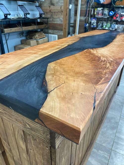 An angled photo of a stylish black epoxy river table by Nautilus Woodcraft.