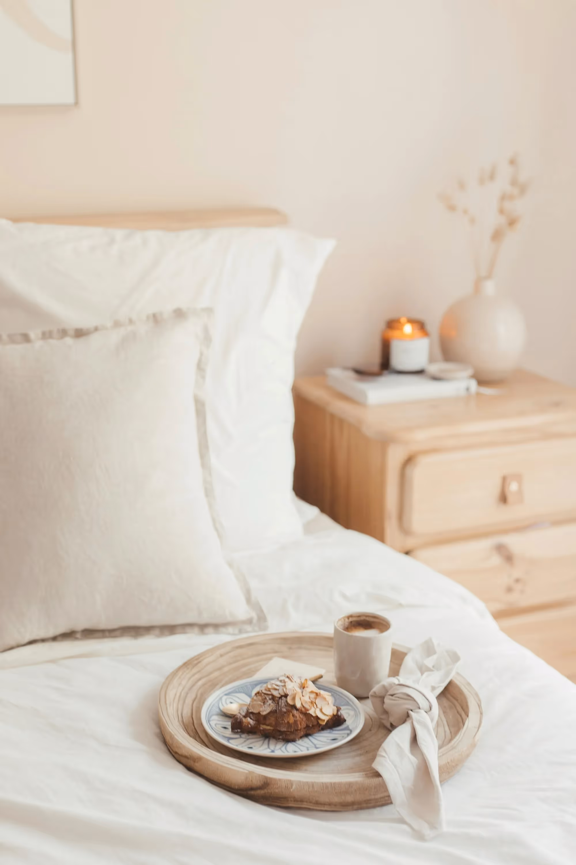 Breakfast tray with a croissant and coffee on a bed with white linens, depicting comfortable living at Crossing at 9th in Salt Lake City.