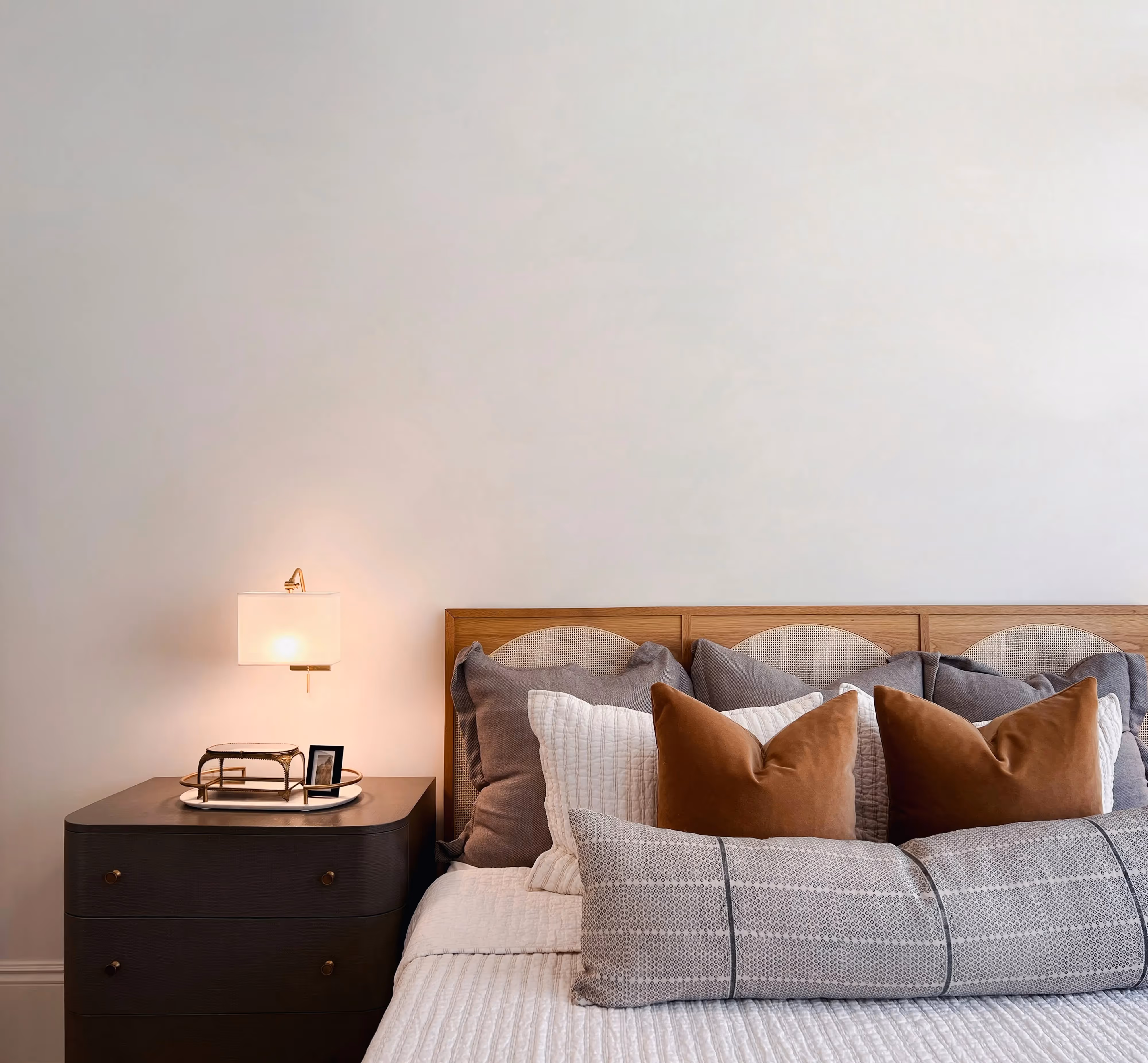 Close-up of a modern bedside table with a lamp and decorative items next to a bed with a wooden headboard, in an apartment at Crossing at 9th in Salt Lake City.