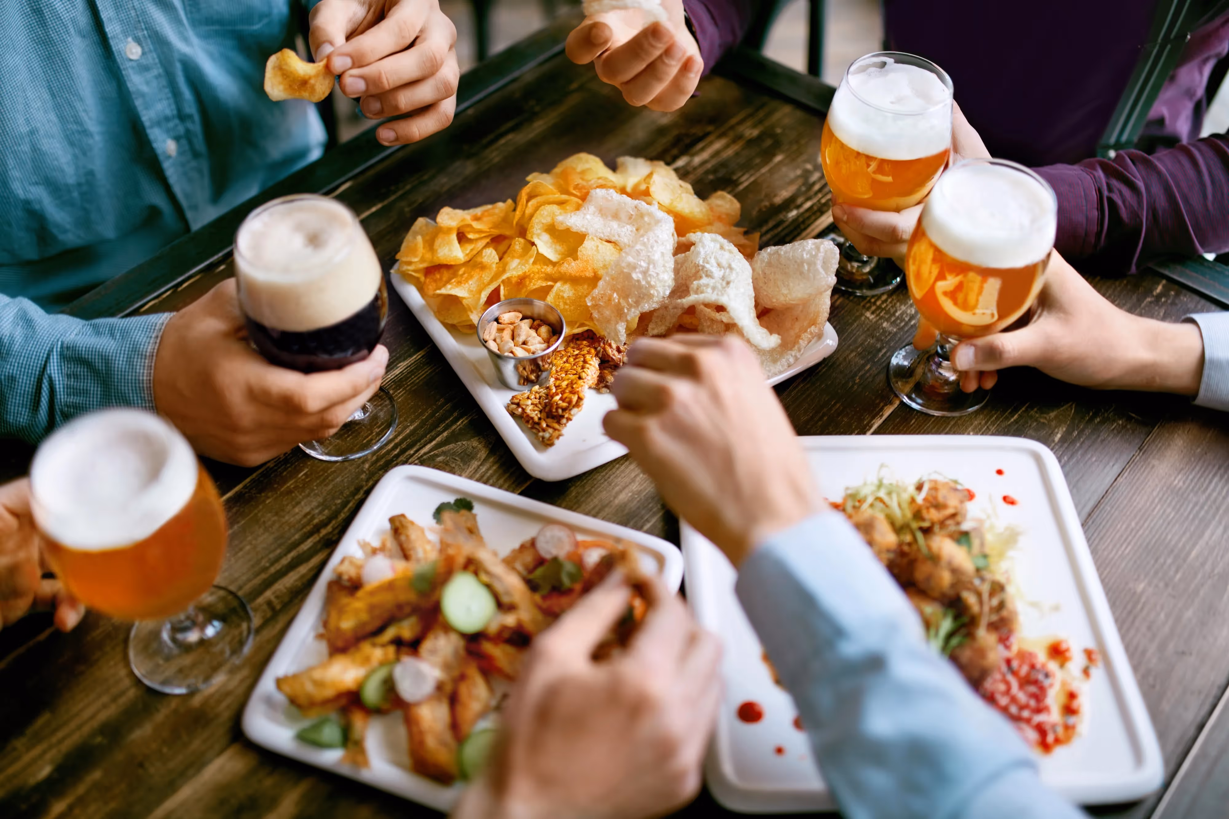 Overhead view of a group of people enjoying craft beers, chips, and small plates at a restaurant, suggesting local dining experiences near Crossing at 9th in Salt Lake City, Utah.