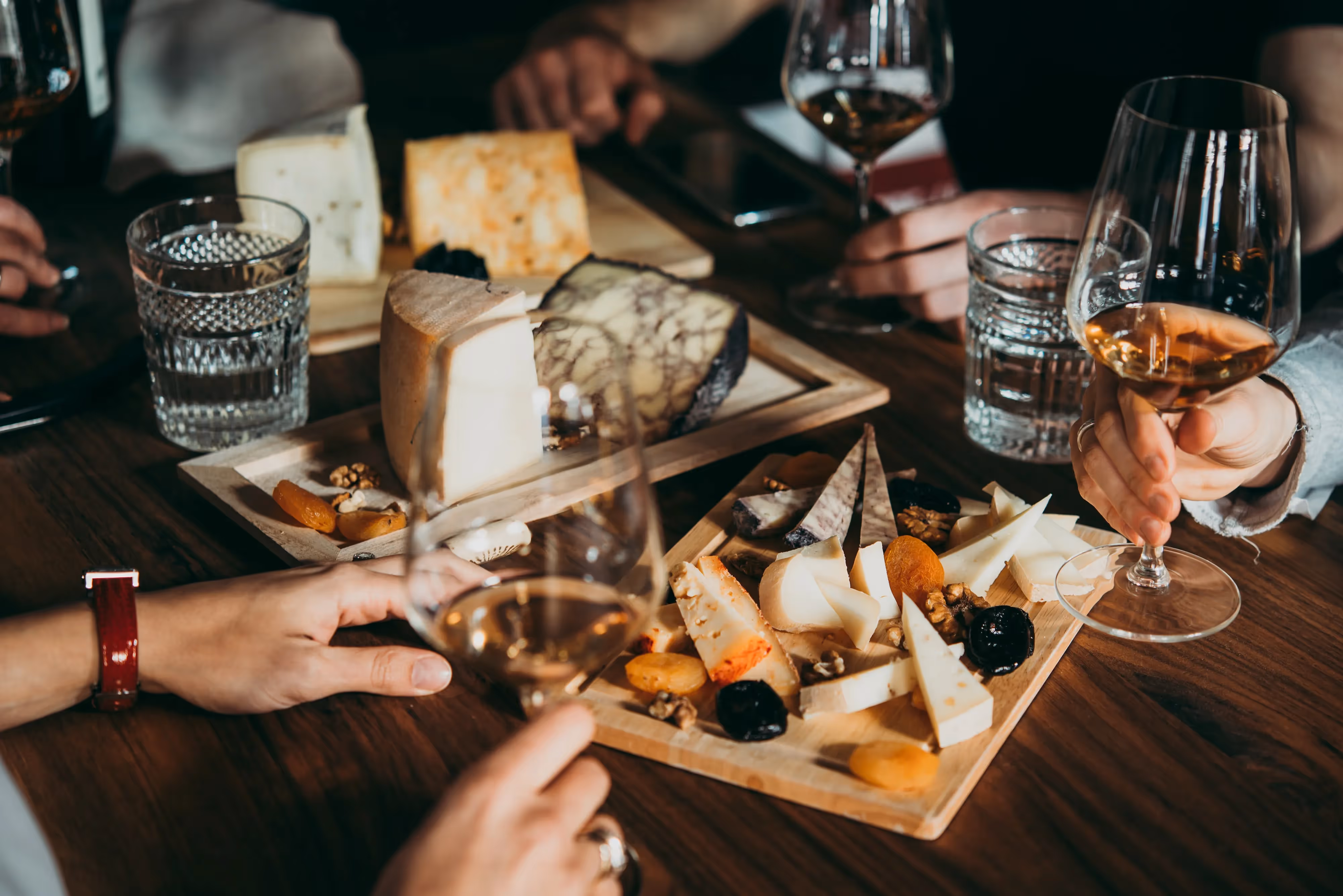 Close-up of a cheese and charcuterie board with wine glasses, enjoyed by a group of people, representing local culinary experiences near Crossing at 9th in Salt Lake City, Utah.