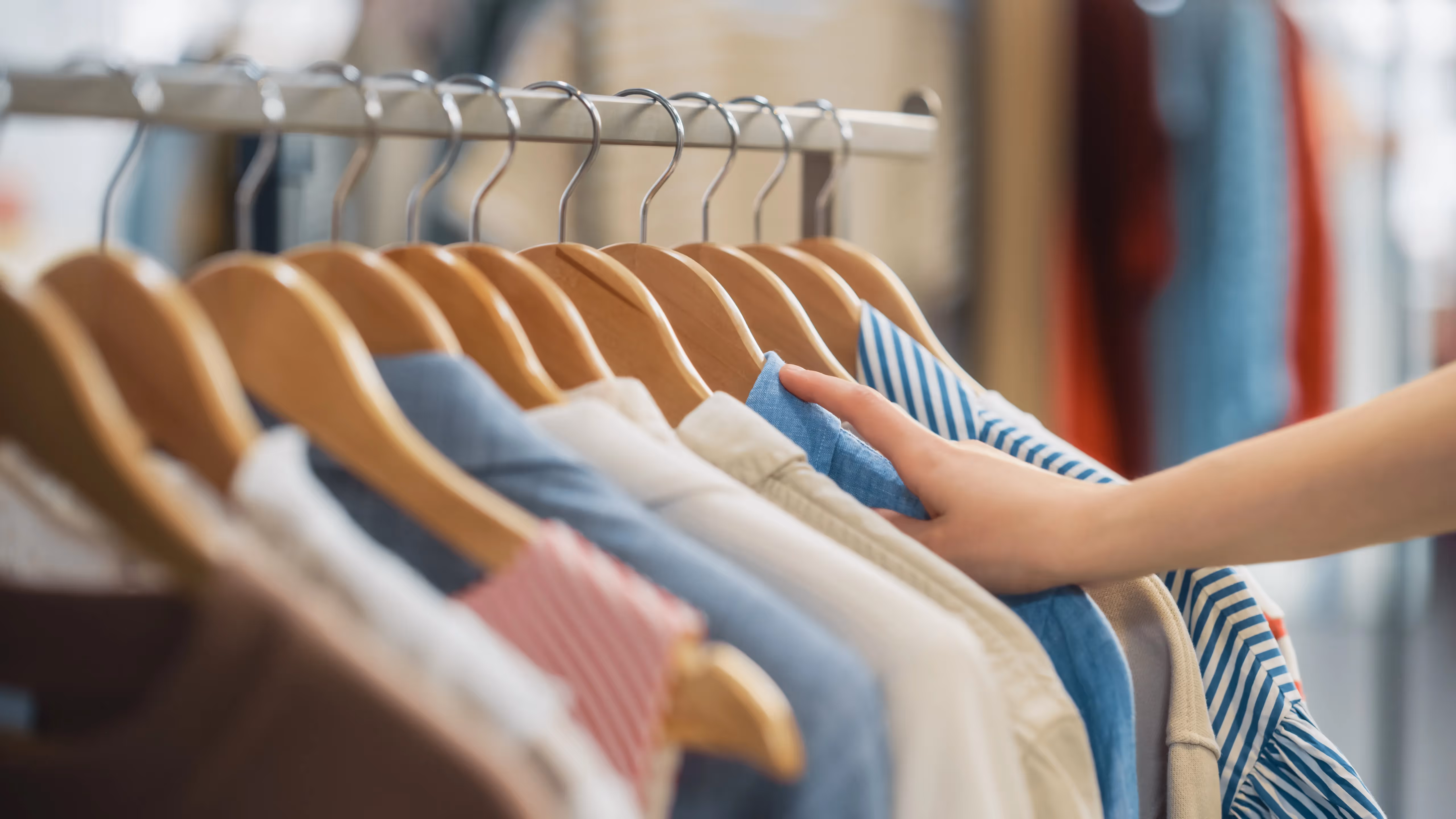 Close-up of a hand Browse through clothes on a rack in a boutique, suggesting convenient shopping experiences near Crossing at 9th in Salt Lake City, Utah.